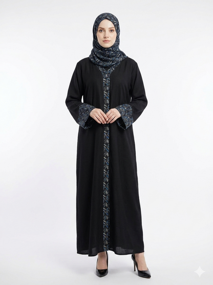 Fair-skinned model with grey eyes wearing a black Nida abaya featuring a blue pashmina-style leaf print on the back, cuffs, and front placket, presented on a solid white background.